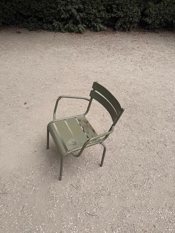 A single green metal chair left alone on the gravel in Luxembourg Gardens.